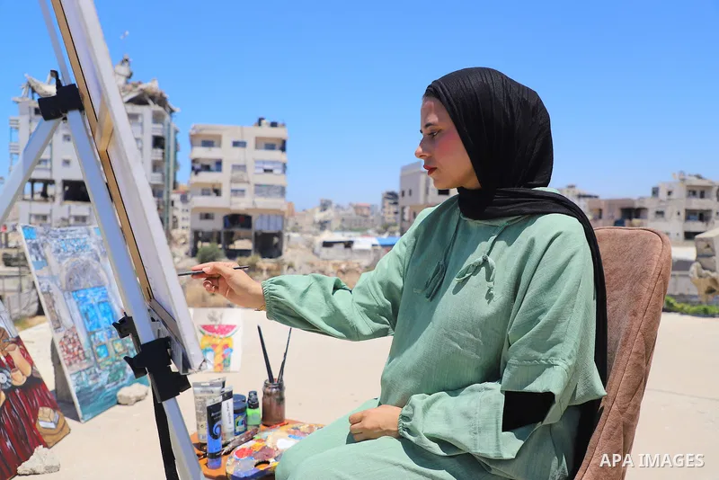 Palestinian visual artist Jana Mahmoud Abu Harbid, 21, paints on the roof of her family's damaged home after returning to northern Gaza and finding her studio destroyed following the war, in Gaza City, on July 20, 2026....
