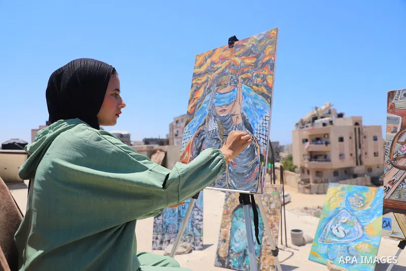 Palestinian visual artist Jana Mahmoud Abu Harbid, 21, paints on the roof of her family's damaged home after returning to northern Gaza and finding her studio destroyed following the war, in Gaza City, on July 20, 2026....