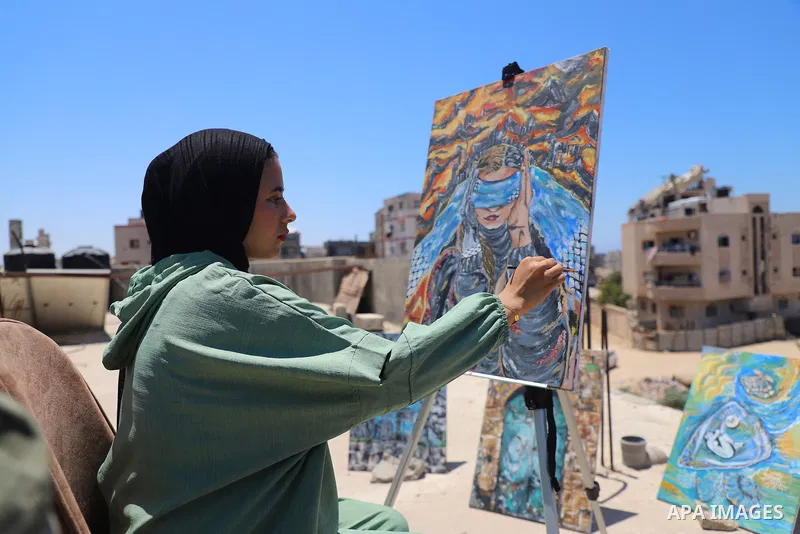 Palestinian visual artist Jana Mahmoud Abu Harbid, 21, paints on the roof of her family's damaged home after returning to northern Gaza and finding her studio destroyed following the war, in Gaza City, on July 20, 2026....
