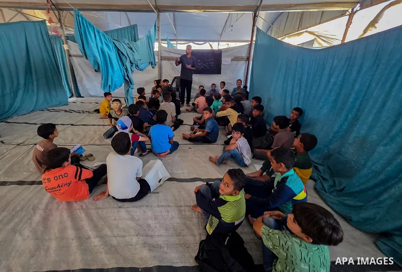 Palestinian children attend classes inside tents at Buthour al-Khair School in Mawasi Khan Younis, southern Gaza Strip, on September 21, 2026, carrying school bags and plastic bags as the new academic year begins. The si...