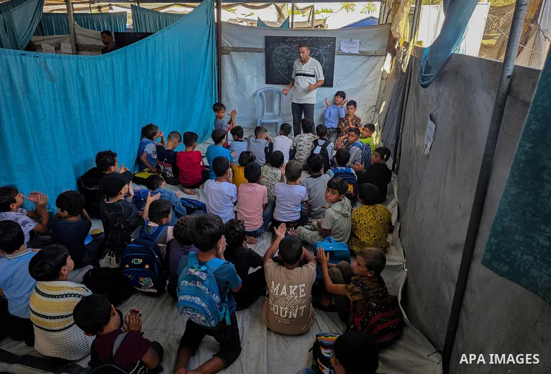 Palestinian children attend classes inside tents at Buthour al-Khair School in Mawasi Khan Younis, southern Gaza Strip, on September 21, 2026, carrying school bags and plastic bags as the new academic year begins. The si...