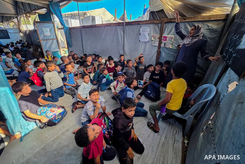 Palestinian children attend classes inside tents at Buthour al-Khair School in Mawasi Khan Younis, southern Gaza Strip, on September 21, 2026, carrying school bags and plastic bags as the new academic year begins. The si...