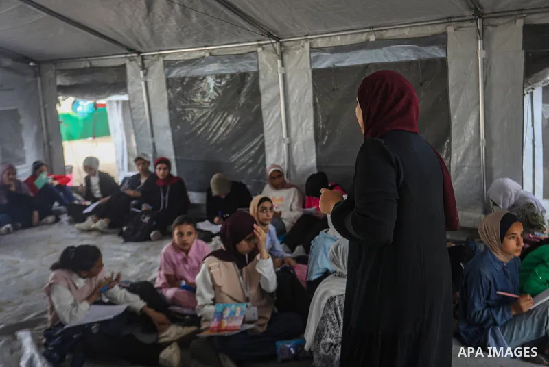 Palestinian students attend classes inside tents at the Saraya education point in the Gaza Strip on October 11, 2026, as education continues under difficult conditions and with shortages of school equipment. Students sit...