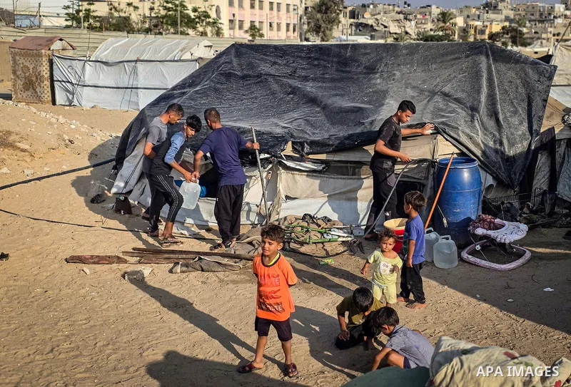 Displaced Palestinian families live in tents inside a cemetery in Khan Younis, in the southern Gaza Strip, on October 14, 2026, and cover them with plastic sheets and tarpaulins to reduce rainwater leakage. The families...