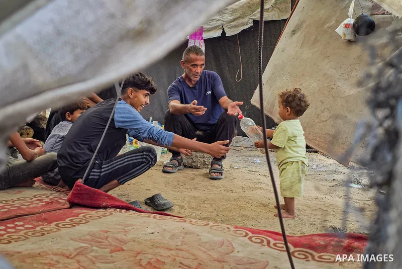 Displaced Palestinian families live in tents inside a cemetery in Khan Younis, in the southern Gaza Strip, on October 14, 2026, and cover them with plastic sheets and tarpaulins to reduce rainwater leakage. The families...