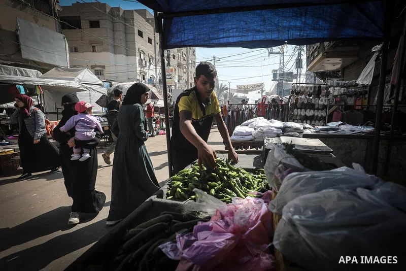 Palestinian vendors and residents stand beside empty fruit and vegetable stalls at a market in the Nuseirat refugee camp, central Gaza Strip, on October 22, 2026, amid severe shortages of fresh produce and record-high pr...