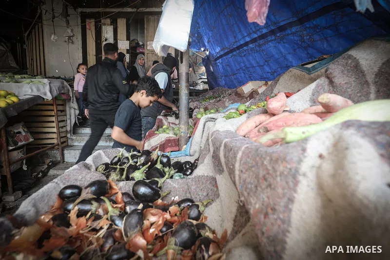 Palestinian vendors and residents stand beside empty fruit and vegetable stalls at a market in the Nuseirat refugee camp, central Gaza Strip, on October 22, 2026, amid severe shortages of fresh produce and record-high pr...