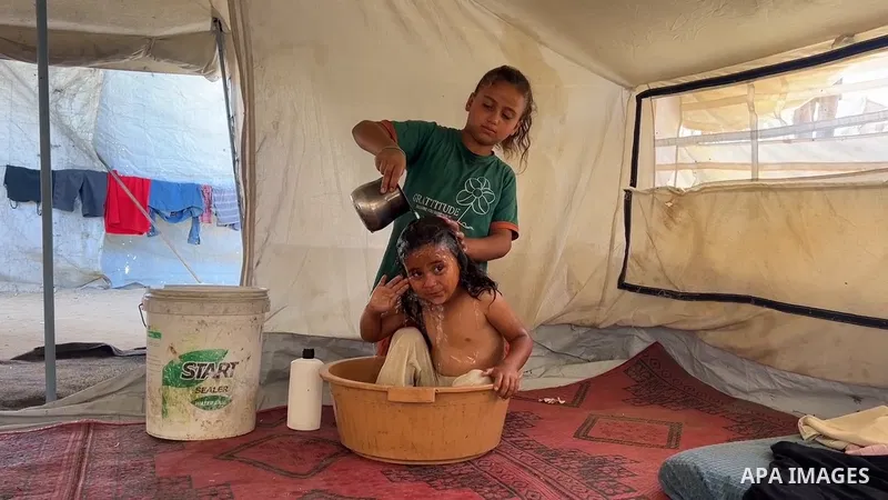 Restrictions Summary: APA wire clients only Shortlist: APAwire - APA wire clients only, Gaza City-Gaza Strip- June 17, 2026. A Palestinian mother bathes her child inside a camp for displaced people in the al-Zawaida area...